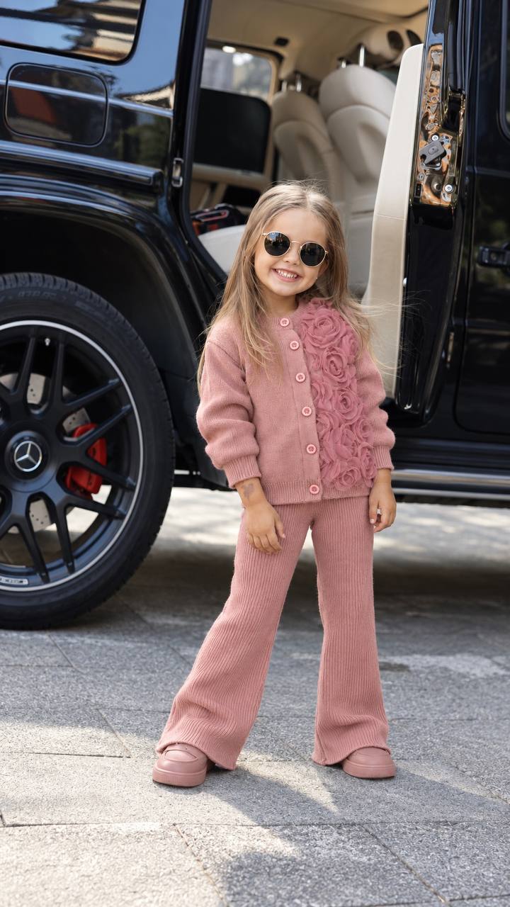 young girl wearing a rose pink knit cardigan and matching pants standing outdoors
